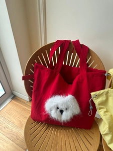 Detail of red canvas tote bag featuring a plush puppy face on a wooden chair