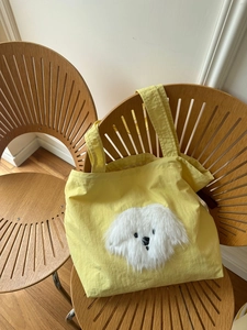 Detail view of yellow tote bag featuring a cute white plush puppy patch on wooden chair