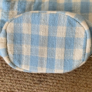 Detail view of oval bottom on blue and white checkered woven handbag with neat stitching