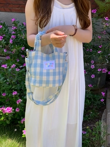 Outdoor lifestyle shot of a blue and white checkered crossbody bag with text patch