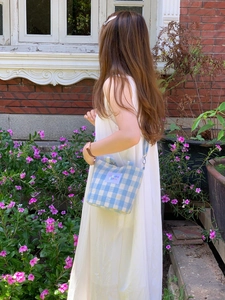 Blue and white plaid crossbody bag styled on a white dress with floral background