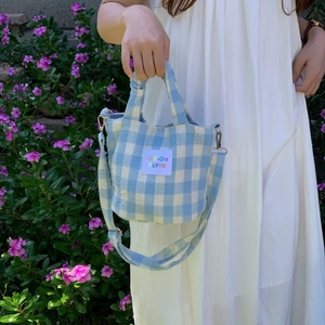 Blue and white gingham plaid handbag with adjustable strap shown in an outdoor setting