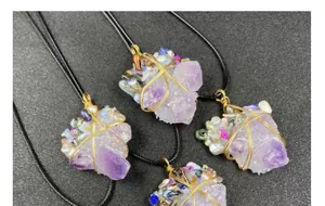 Close-up of handmade amethyst raw stone pendant with gold wire wrap and pearl accent