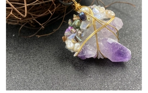 Macro shot of handmade amethyst crystal pendant with wire wrap and pearl details
