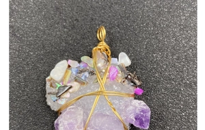 Macro view of handmade wire wrapped amethyst and pearl pendant with intricate gold details