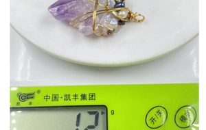 Detail shot of a handmade amethyst wire wrapped pendant on a digital scale weighing 12.1g