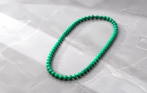 Macro detail of malachite bead necklace with natural green textures on a grey neck bust