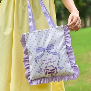 Close-up of lavender canvas tote with Chupa Chups logo and frill edge on a green lawn