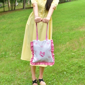 Detail of pink ruffled edges and cherry bow print on white striped canvas tote bag