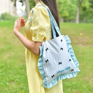 Detail of blue striped tote bag with ruffled edges and bow prints in outdoor setting