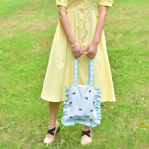 Detail of light blue canvas tote bag with ruffled edges and cute bow embroidery