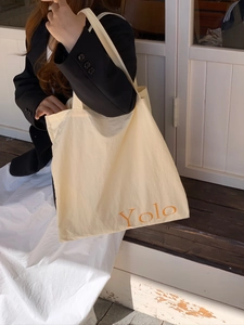 Detail einer beigen Canvas-Tasche mit orangefarbenem YOLO-Text und einem Model im Blazer