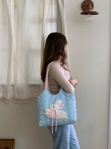 Detail of blue quilted tote bag with heart embroidery and plush bunny on shoulder