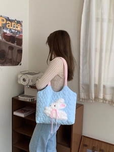 Detail of light blue quilted tote bag with white plush rabbit and pink shoulder strap