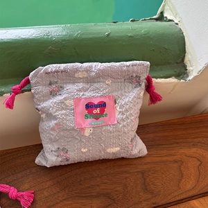 Dettaglio della borsa in tessuto a bolle azzurro con etichetta rosa e coulisse a nappe