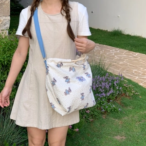 Detail of quilted off-white tote bag featuring cartoon bear patterns and blue shoulder strap