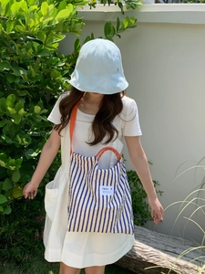 Detail of blue and yellow striped canvas bag with orange strap and white woven label