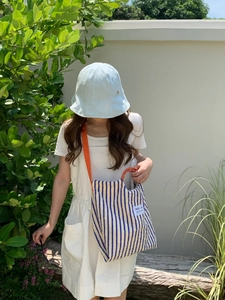 Outdoor shot of a striped canvas bag with bright orange straps and blue fisherman hat