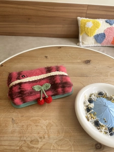 Détail d'une trousse à maquillage en peluche à carreaux roses avec cerise crochetée