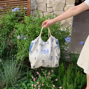Off-white canvas tote bag with blue teddy bear prints and outdoor floral garden background
