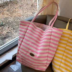 Detail of colorful striped canvas tote bag with metal brand tag in a cozy indoor setting