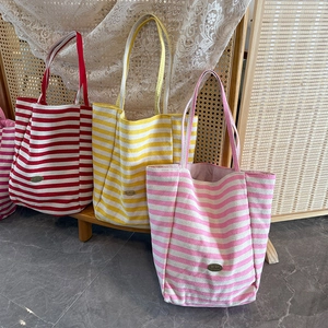 Detailed view of three striped canvas tote bags in red, yellow, and pink on a bench