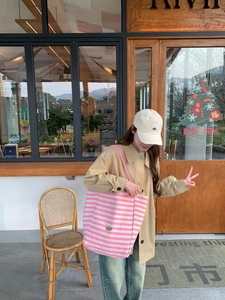 Detail of pink and white striped canvas tote bag worn with casual beige trench coat