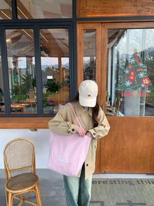 Pink striped canvas tote bag with Faith mole text detail worn with a beige trench coat