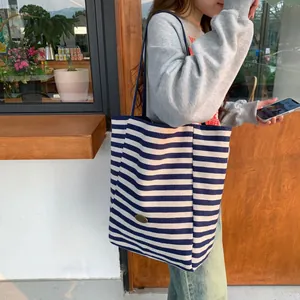 Detail of blue and white striped canvas tote bag with a handmade metal plate on shoulder