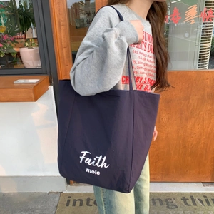 Detail of navy blue canvas tote bag with white Faith mole script shown in outdoor setting
