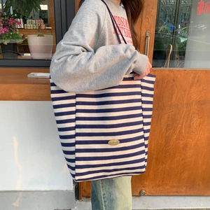 Detail of blue and white striped canvas tote with a handmade metal tag on a spacious bag