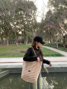 Outdoor shot of a model wearing a large beige and brown striped canvas tote bag