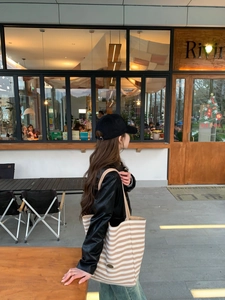 Detail of a large striped canvas tote bag styled with a leather jacket and baseball cap