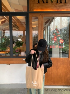 Outdoor shot of light brown canvas tote bag with Faith text and black leather jacket