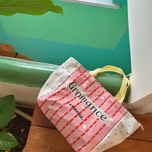 Canvas tote bag with yellow pink plaid design and letter print on wooden surface