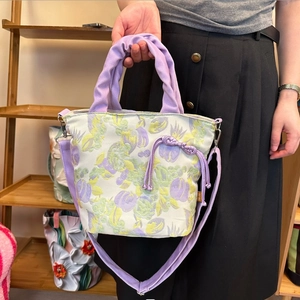 Dettaglio della borsa a secchiello in tela floreale con manici viola arricciati e coulisse