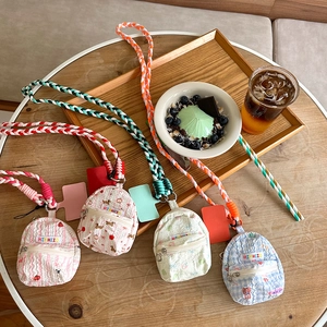 Mini backpack-shaped coin purses in four colors with braided lanyards on a wooden table