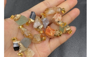 Mano sosteniendo colgantes de cristal natural con bordes dorados y formas únicas