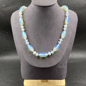 Détail du collier de perles en opale bleue translucide sur un buste gris foncé