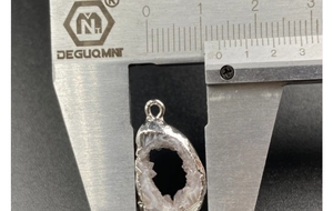 Macro detail of natural geode pendant being measured with a silver caliper tool