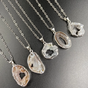 Natural Brazilian agate geode pendant necklaces with silver chains on black sand background