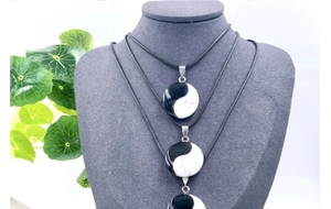 Detailed view of three Yin Yang stone pendants on black cords displayed on a model stand