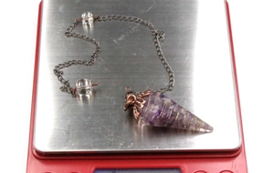 Macro shot of amethyst crystal pendulum with gold wire wrapping on red electronic scale