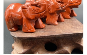 Detailopname van handgesneden olifantbeeldjes van rode steen op een houten onderstel