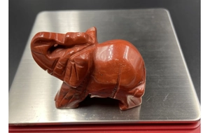 Detailweergave van een handgesneden olifantenbeeldje van rode jaspis op een weegschaal