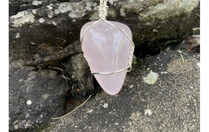 Détail d'un pendentif en quartz rose enveloppé de fil métallique sur une pierre naturelle