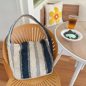 Blue and grey striped plush tote bag in a cozy autumn cafe setting on a wooden chair