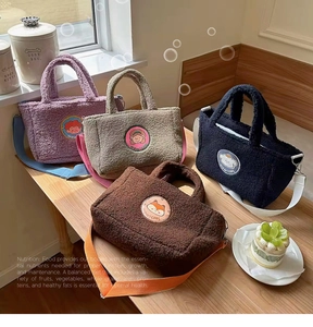 Detailed view of four colorful teddy fleece tote bags with cartoon patches on a wooden table