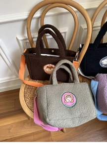 Detail view of colorful lamb wool tote bags with cartoon embroidery on a wooden chair