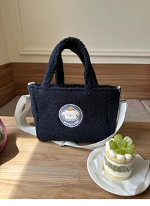 Close-up of black lamb wool tote bag featuring a cute puppy embroidery on a wooden table